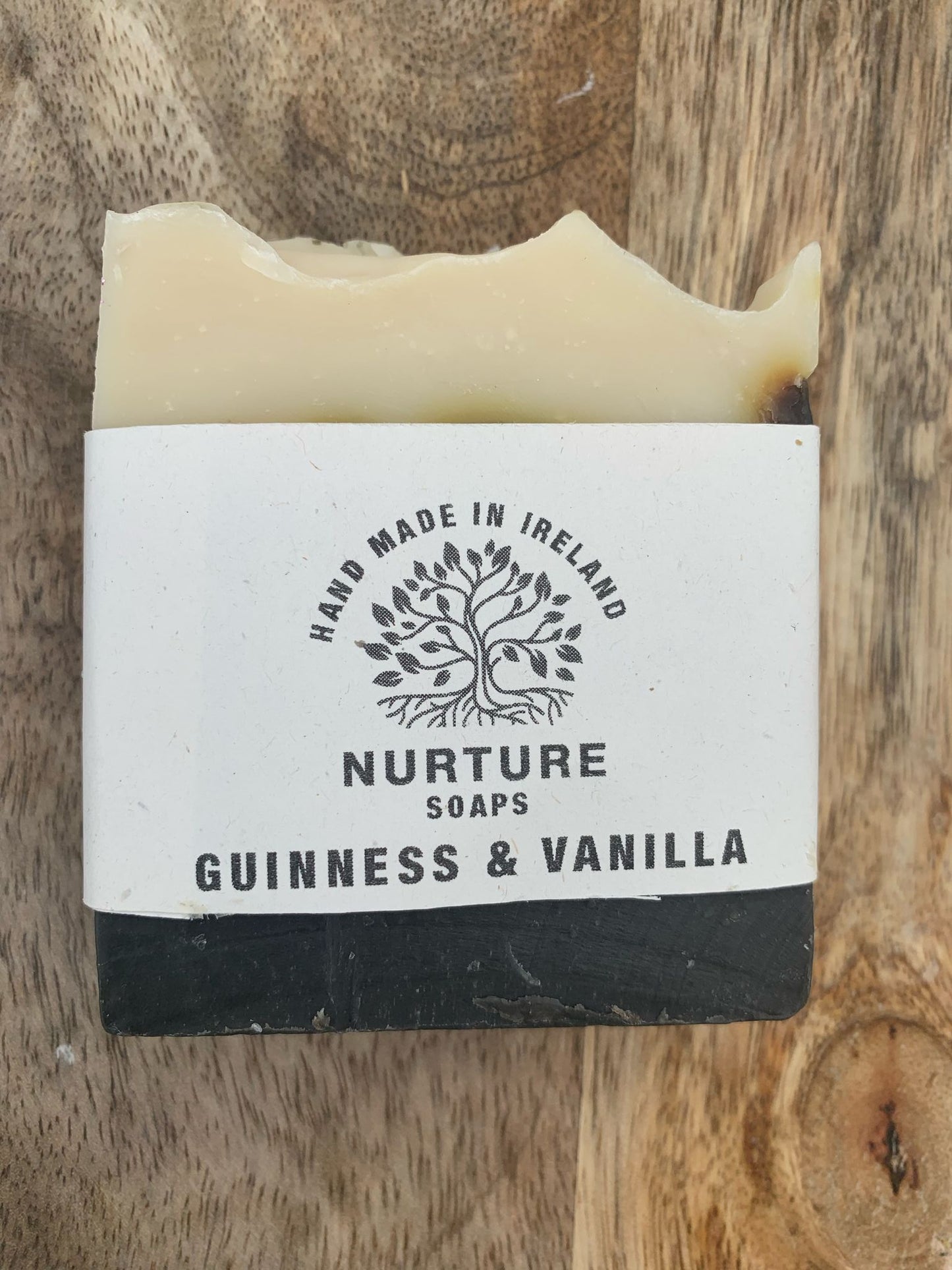 A bar of Guinness and Vanilla soap with a label that reads 'NURTURE SOAPS - GUINNESS & VANILLA'. The soap is placed on a wooden surface.