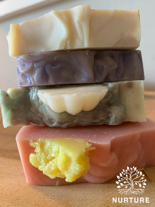 A stack of three bars of soap with varying shades of purple, green, and pink, with the Nurture logo on the bottom right.
