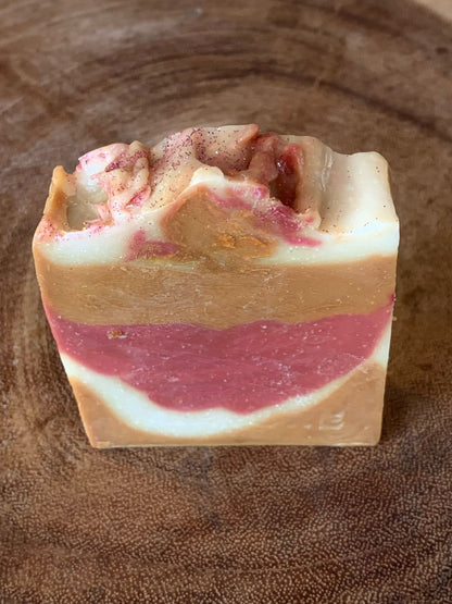 A bar of soap with layers of beige and pink, topped with a sprinkle of pink powder, on a wooden surface.