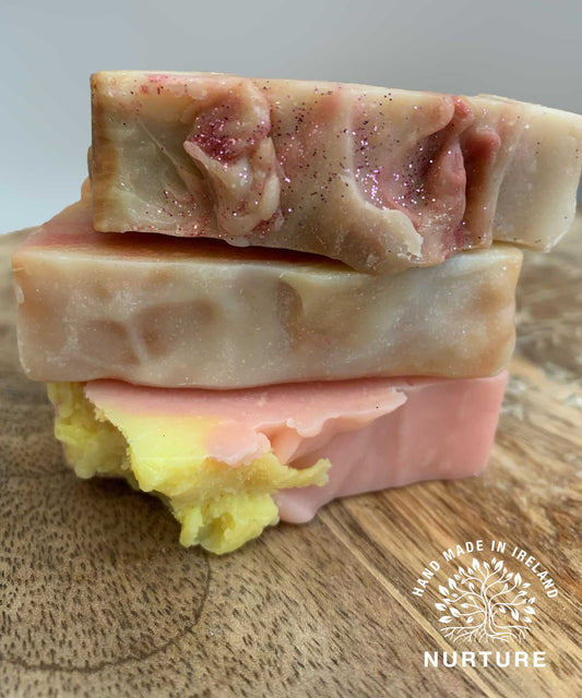 A set of handmade soaps with varying shades of pink, orange, and beige, featuring visible exfoliants.
