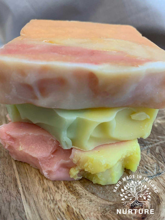 A stack of colorful handmade soaps with a watermarked logo on the bottom right, indicating the brand.